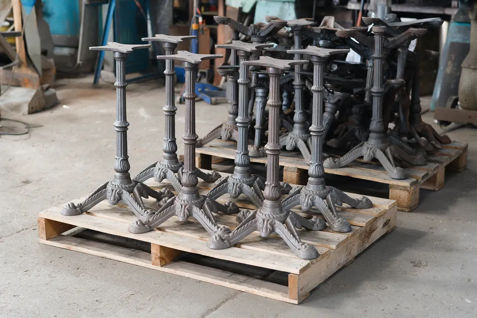 Illustrative image (not a Belmont job): Cast iron pedestal table bases sandblasted to a natural metal patina, on pallets ready for shipping